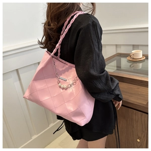 Pink quilted tote bag with pearl chain detail and woven handle shown on model