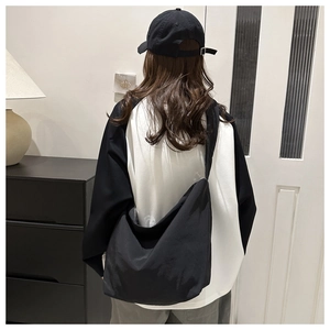 Rear view of minimalist black large capacity crossbody bag worn by a model in casual setting