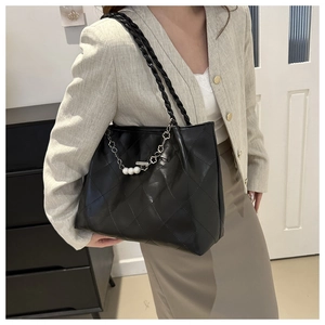 Detail of black quilted tote bag featuring elegant pearl chain and woven handles