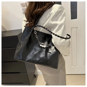 Detail of black quilted tote bag with woven shoulder strap and pearl chain charm