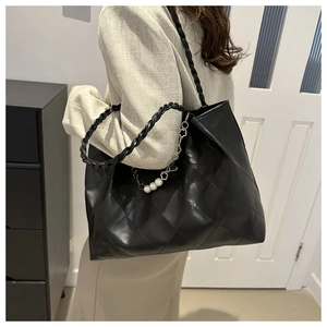 Detail of black quilted tote bag with pearl decorative chain and woven handles