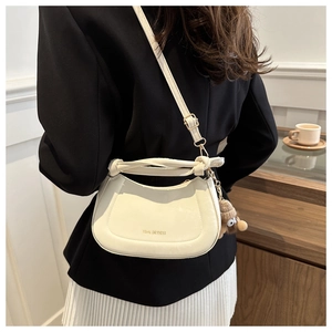 Detail of cream leather crossbody bag featuring leather knot handle and plush monster charm