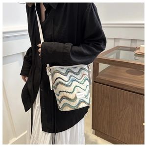 Detail of crochet bucket bag with wave patterns and white leather shoulder strap on a model