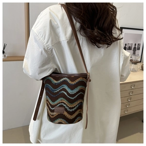 Detail of hand-woven bucket bag with colorful wavy patterns and leather strap