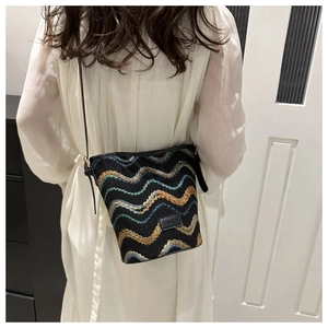 Detail of a woven bucket bag featuring colorful wave embroidery and a fashion label