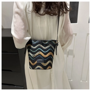 Detail of embroidered wave pattern on black bucket bag worn with white dress