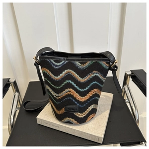 Detail showing zigzag woven pattern and leather 'FASHION' label on black bucket bag