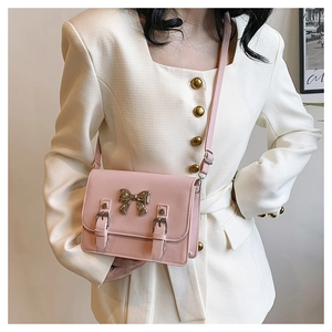 Detail of light pink crossbody bag with metal bow accent and leather straps