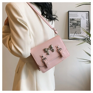 Close-up of pink crossbody bag with metal bow decoration and silver buckle detail