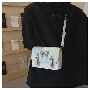 Detailed side view of light green crossbody bag with silver bow accent and adjustable strap