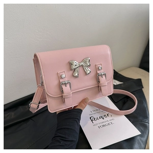 Close-up of pink crossbody bag featuring a silver metal bow and decorative buckle straps