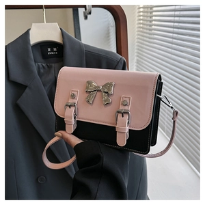 Detail of pink and black crossbody bag featuring a silver metal bow and buckle straps
