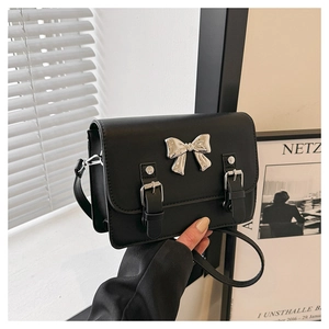 Detail of black crossbody bag with silver bow hardware and buckled straps