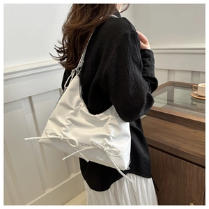 Détail du sac à bandoulière blanc plissé avec nœuds porté par un mannequin en café