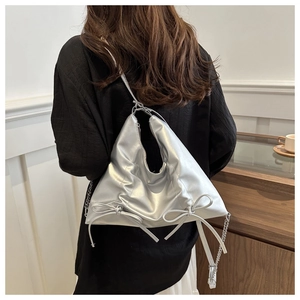 Détail d'un sac à bandoulière argenté avec nœud et plis porté par un mannequin
