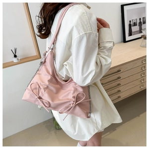 Détail d'un sac à épaule en nylon rose avec nœuds porté par un mannequin