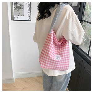 Détail d'un sac cabas en toile à carreaux roses avec étiquette porté par le mannequin