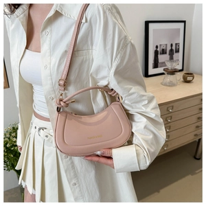 Sac bandoulière demi-lune rose pâle avec lettrage doré dans un décor intérieur cosy