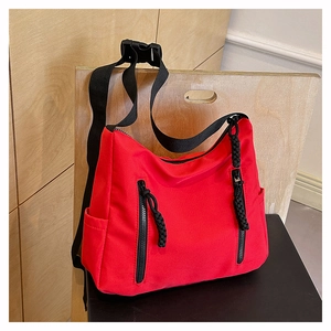 Detail of red nylon crossbody bag featuring black vertical zippers and woven pullers