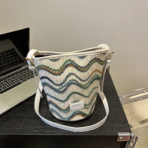 Fashion woven bucket bag with wave embroidery and leather strap on a desk background