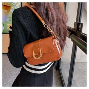 Sac sous le bras marron motif crocodile avec chaîne dorée porté par un modèle