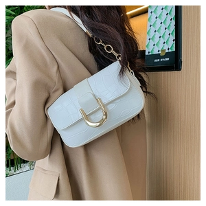 Détail du sac sous le bras blanc motif croco avec boucle D dorée et bandoulière chaîne
