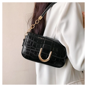 Détail du sac sous le bras noir motif crocodile avec boucle en U dorée et bandoulière chaîne