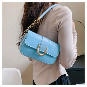 Détail du sac bleu clair à texture crocodile avec boucle en U dorée et bandoulière chaîne