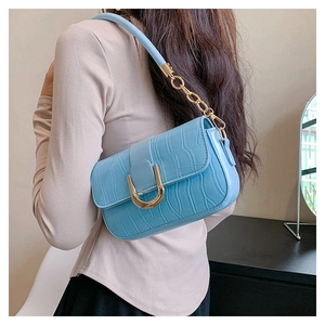 Détail d'un sac sous le bras bleu clair motif crocodile avec boucle dorée et bandoulière chaîne