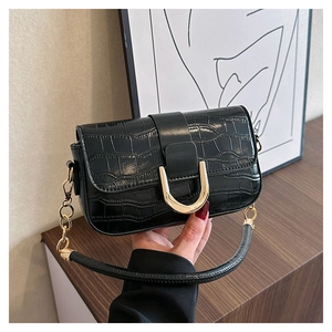 Détail d'un sac noir à motif crocodile avec boucle dorée en U et bandoulière en chaîne