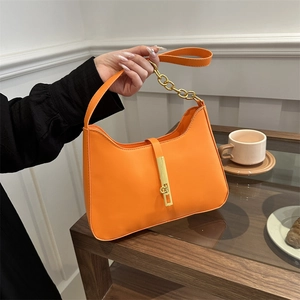 Orange minimalist hobo shoulder bag with gold chain and metal buckle in lifestyle setting