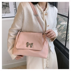 Detail of pink shoulder bag featuring a golden bow accent and chain strap worn by a model