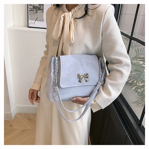 Close-up of light blue flap bag with golden bow clasp and chain strap detail