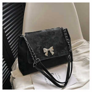 Detail of black suede shoulder bag featuring a silver metal bow and chain strap