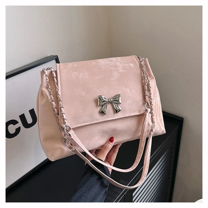 Close-up of pink suede shoulder bag featuring a silver metal bow and chain straps