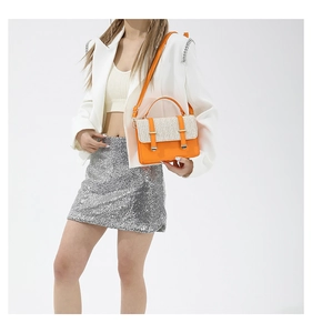 Detail of a stylish orange leather and straw crossbody bag with metal buckles on a model