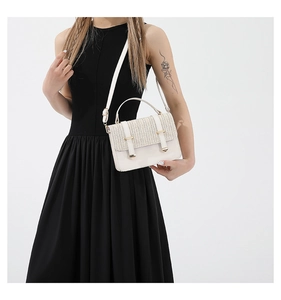 Detail of cream crossbody bag featuring straw woven flap and gold metal buckle clasp