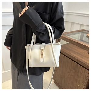 Macro detail of a minimalist white crossbody tote bag with golden metal twist lock closure