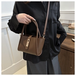 Close-up of brown matte leather tote bag with gold rectangular clasp on a model