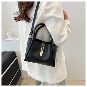 Detail of a black minimalist tote bag with gold metal twist lock on a white blazer