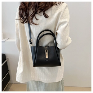 Modern black minimalist tote bag carried by a model in a white suit against a clean background