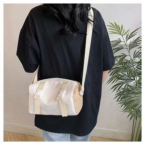 Close-up of cream cylindrical crossbody bag showing adjustable strap and buckle details