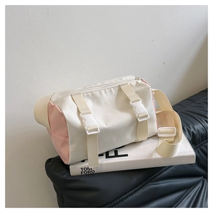 Detail of canvas barrel crossbody bag featuring pink and cream patchwork with buckles
