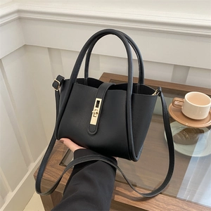 Minimalist black leather tote bag with gold metal clasp on an elegant cafe table