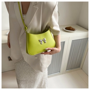 Detail of lime green crossbody bag with silver bow ornament on white blazer outfit