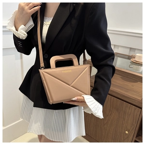 Detail of a beige handbag featuring geometric creases and a sleek metal top handle