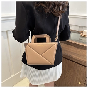 Detail van de beige crossbodytas met geometrische vouw en metalen logo op de tas