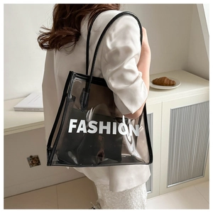 Close-up of a large smoke grey transparent PVC tote bag with white FASHION print and black pouch