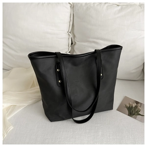 Minimalist black tote bag with gold rivets and dual straps on white textile background
