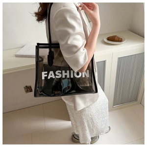 Detail view of large transparent PVC tote bag with black leather trim and FASHION lettering
